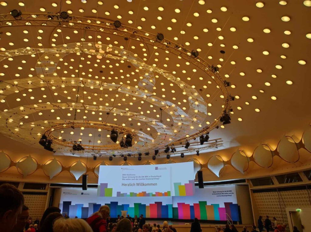 Blick in den Saal mit Begrüßungstext an der Leinwand