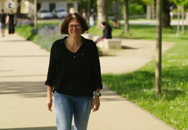 Eine Frau mit dunklen Haaren, einer Brille, einemn schwarzen Hemd und blauer Jeans