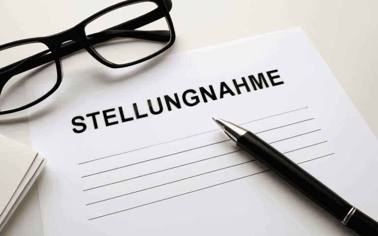 Ein weißes Blatt Papier auf dem Stellungnahme steht und daneben liegen ein Kugelschreiber und eine Brille